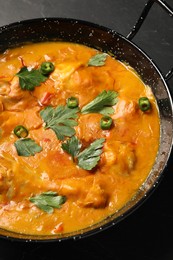 Photo of Tasty chicken curry with parsley and pepper on black table
