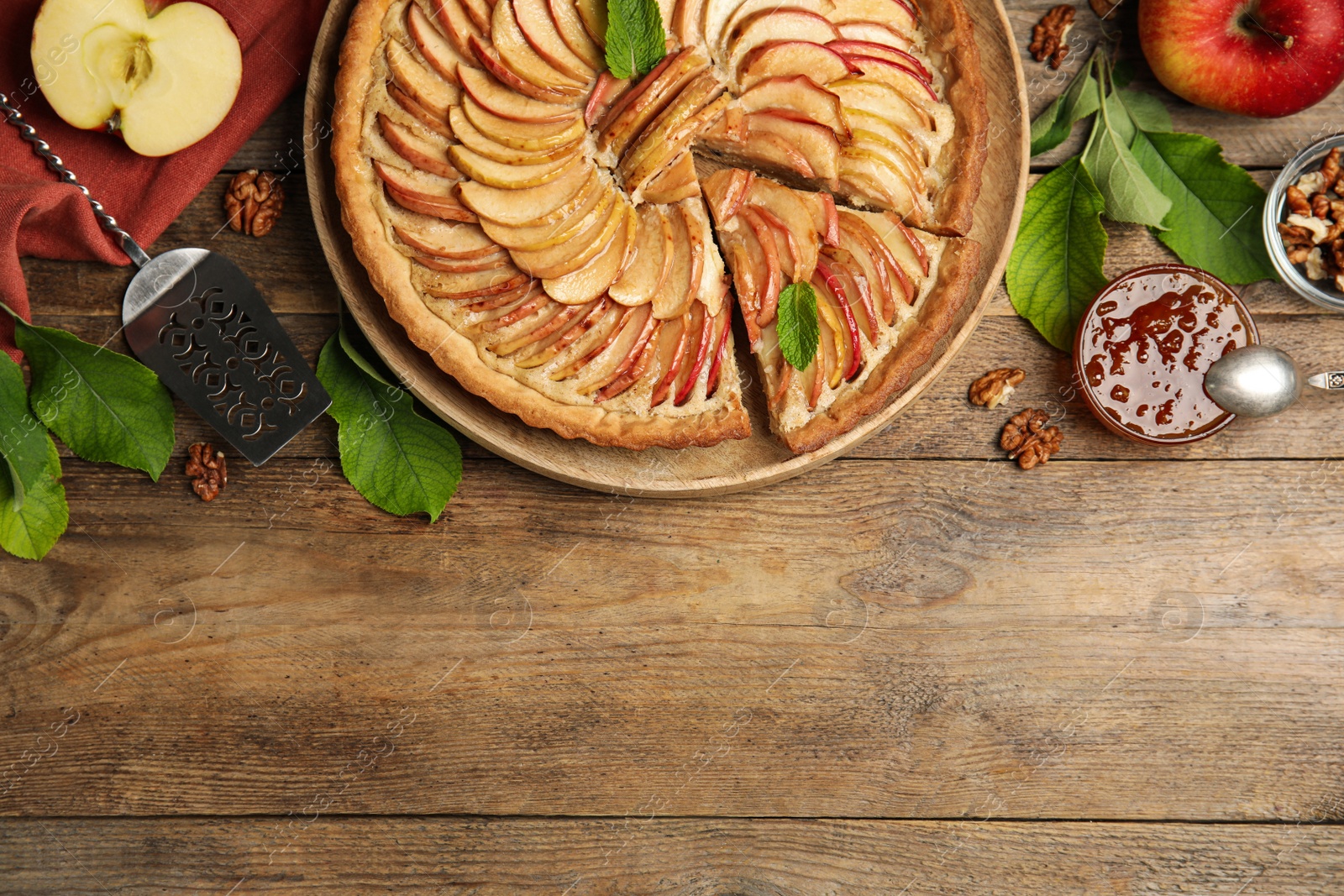 Photo of Delicious apple pie and ingredients on wooden table, flat lay. Space for text