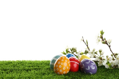 Painted Easter eggs and blossoming branches on green grass against white background