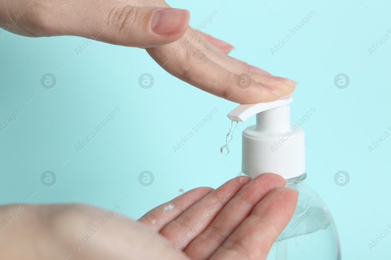 Photo of Woman applying antiseptic gel on hand against light blue background, closeup