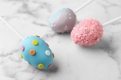 Egg shaped cake pops for Easter celebration on white marble table, closeup