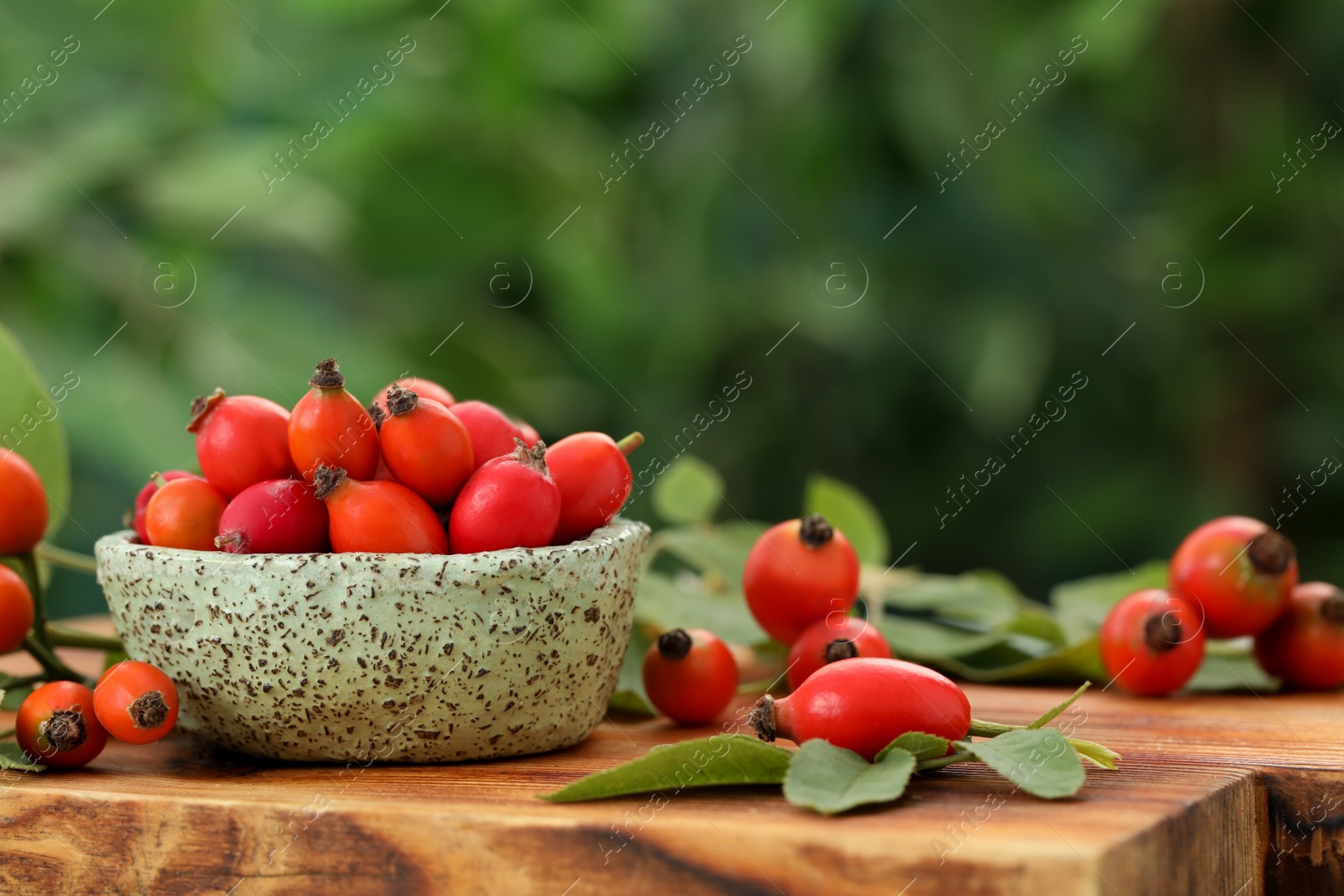 Photo of Ripe rose hip berries with green leaves on wooden table. Space for text