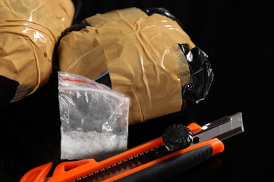Photo of Smuggling, drug trafficking. Packages with narcotics and utility knife on black surface, closeup