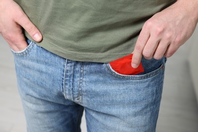 Man pulling condom out of pocket on blurred background, closeup