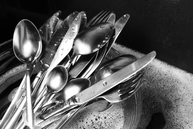 Photo of Washing silver spoons, forks and knives in kitchen sink with foam, closeup