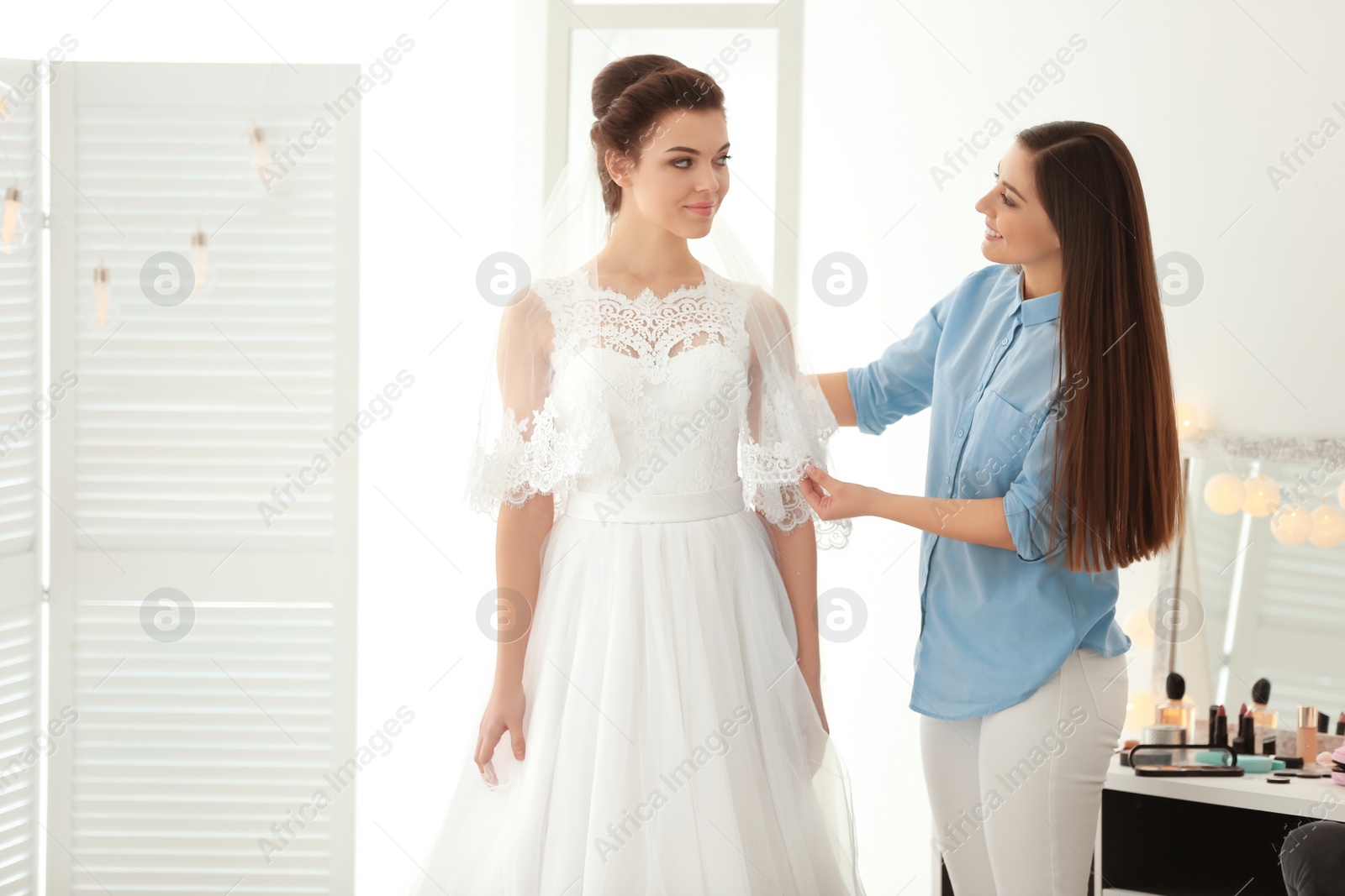 Photo of Fashion stylist preparing bride before her wedding in room