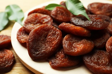 Photo of Plate of tasty apricots and green leaves on wooden table, closeup. Dried fruits