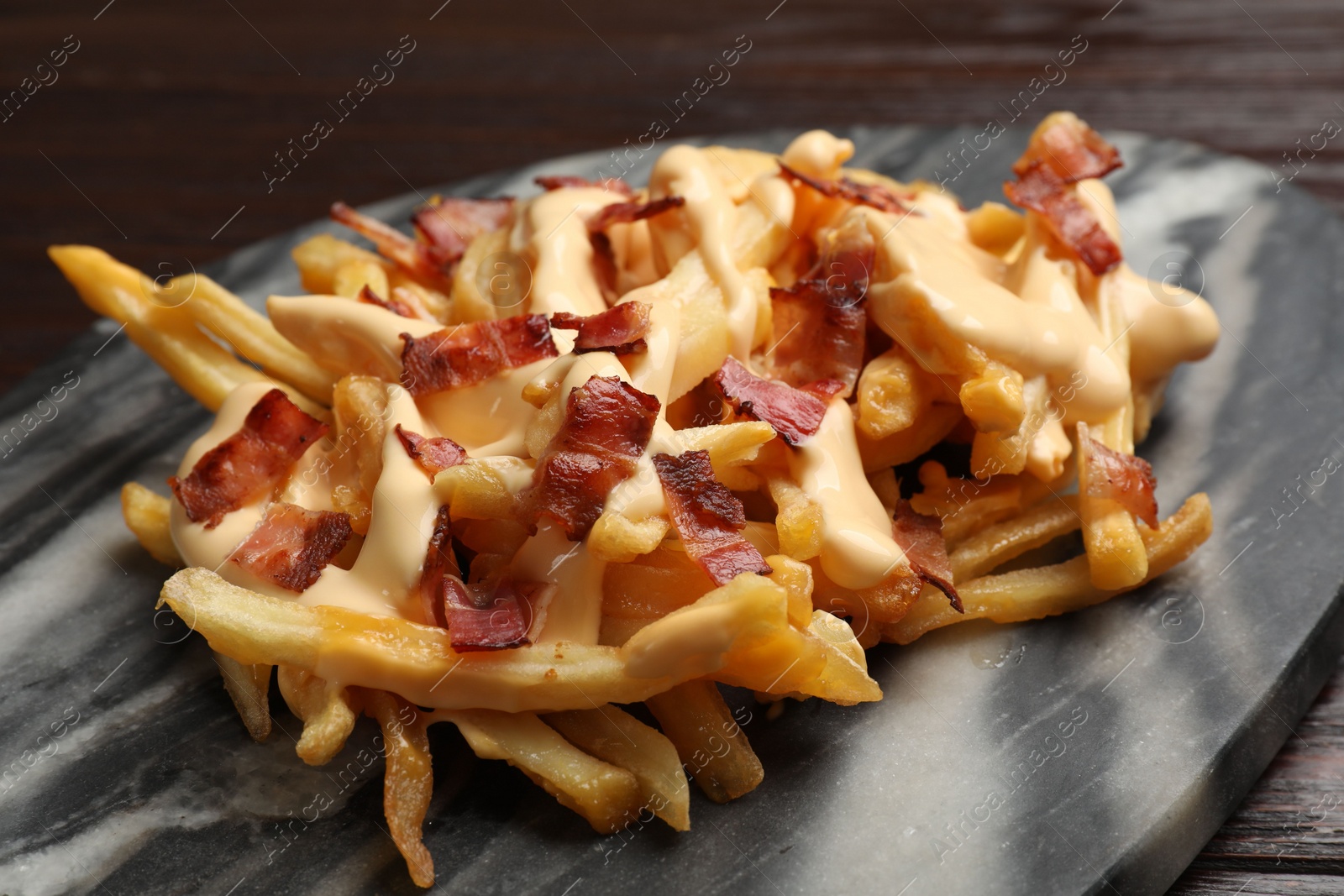 Photo of Delicious French fries with bacon and cheese sauce on table, closeup