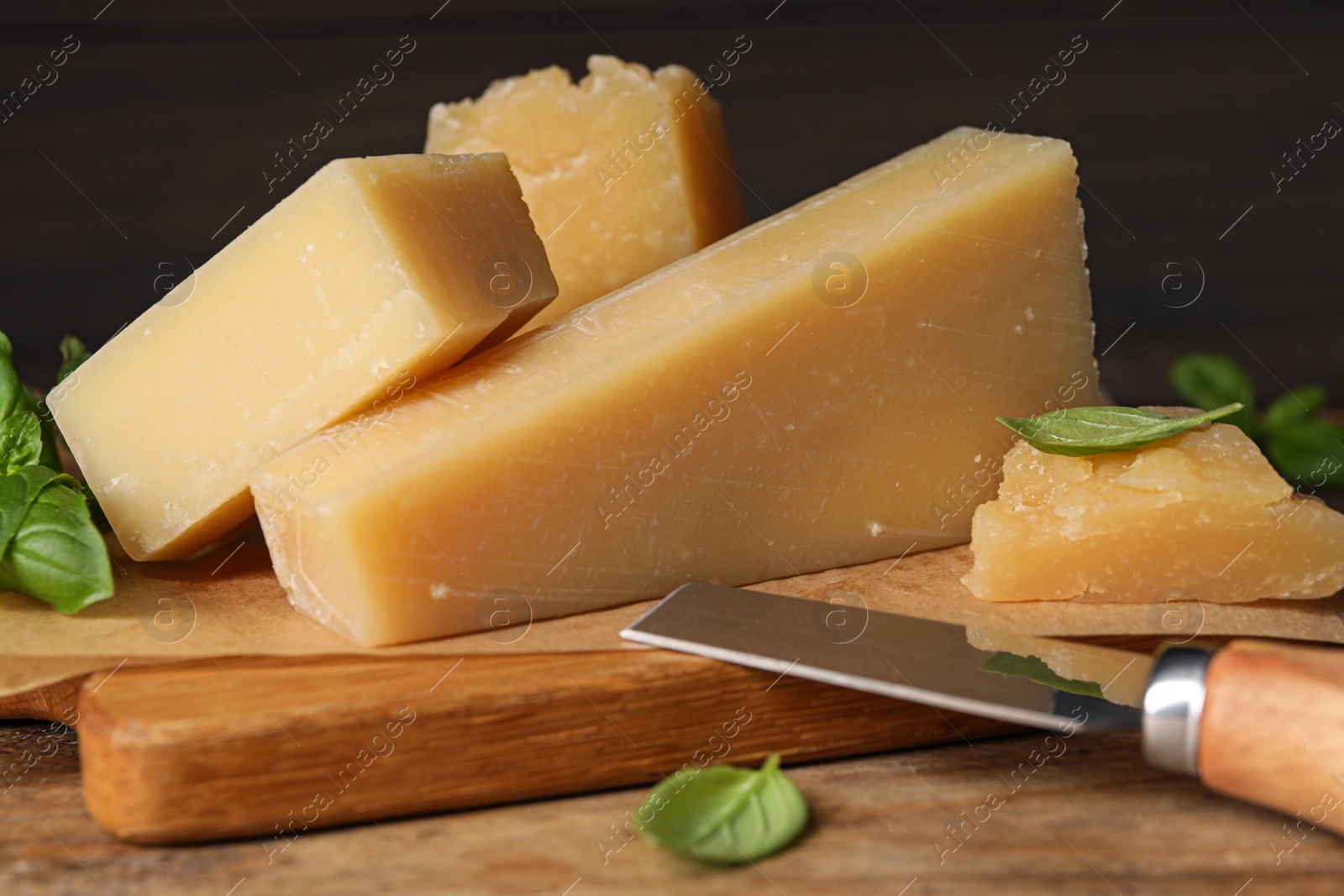 Photo of Delicious parmesan cheese with basil and knife on wooden table, closeup