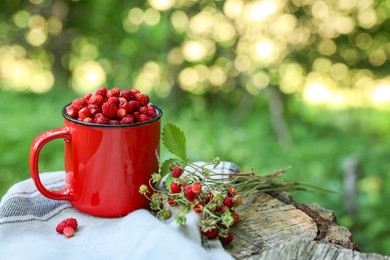 Photo of Mug and tasty wild strawberries on stump against blurred background. Space for text