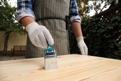 Photo of Man varnishing wooden surface with brush outdoors, closeup