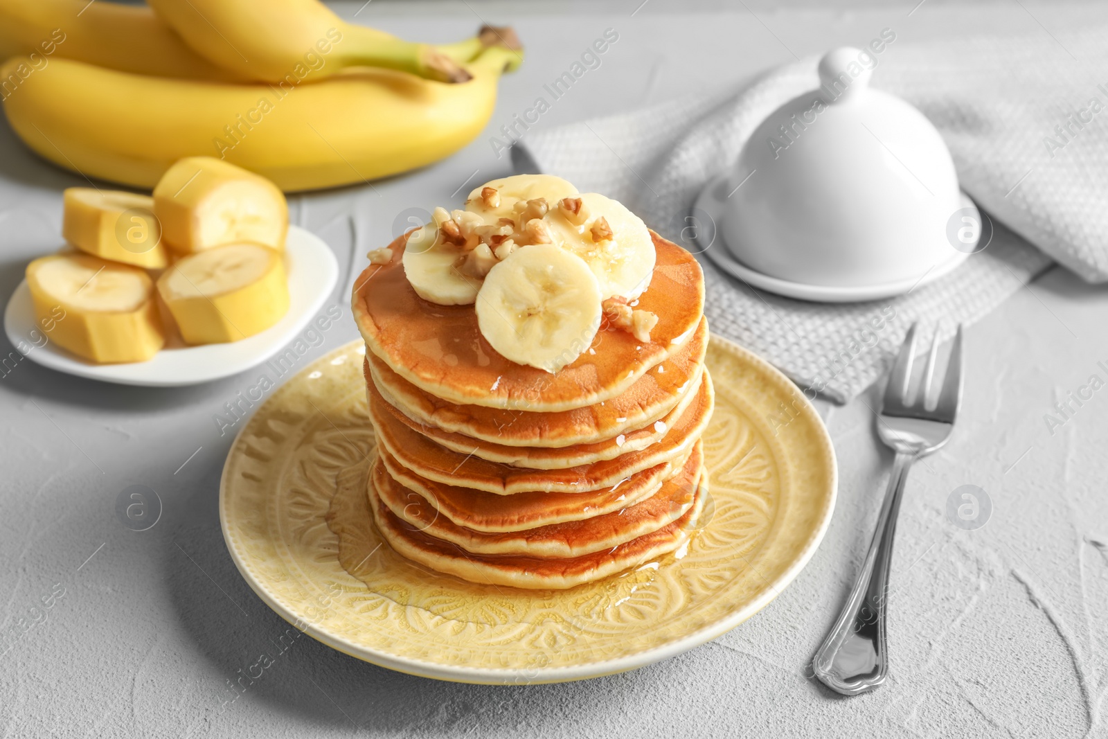 Photo of Stack of tasty pancakes with banana, nuts and honey on table