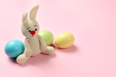 Photo of Cute Easter bunny toy and dyed eggs on color background, space for text