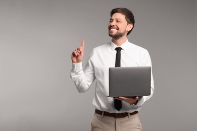 Photo of Happy man with laptop on grey background. Space for text