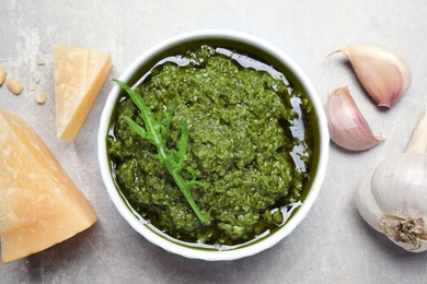 Bowl of tasty arugula pesto and ingredients on light table, flat lay