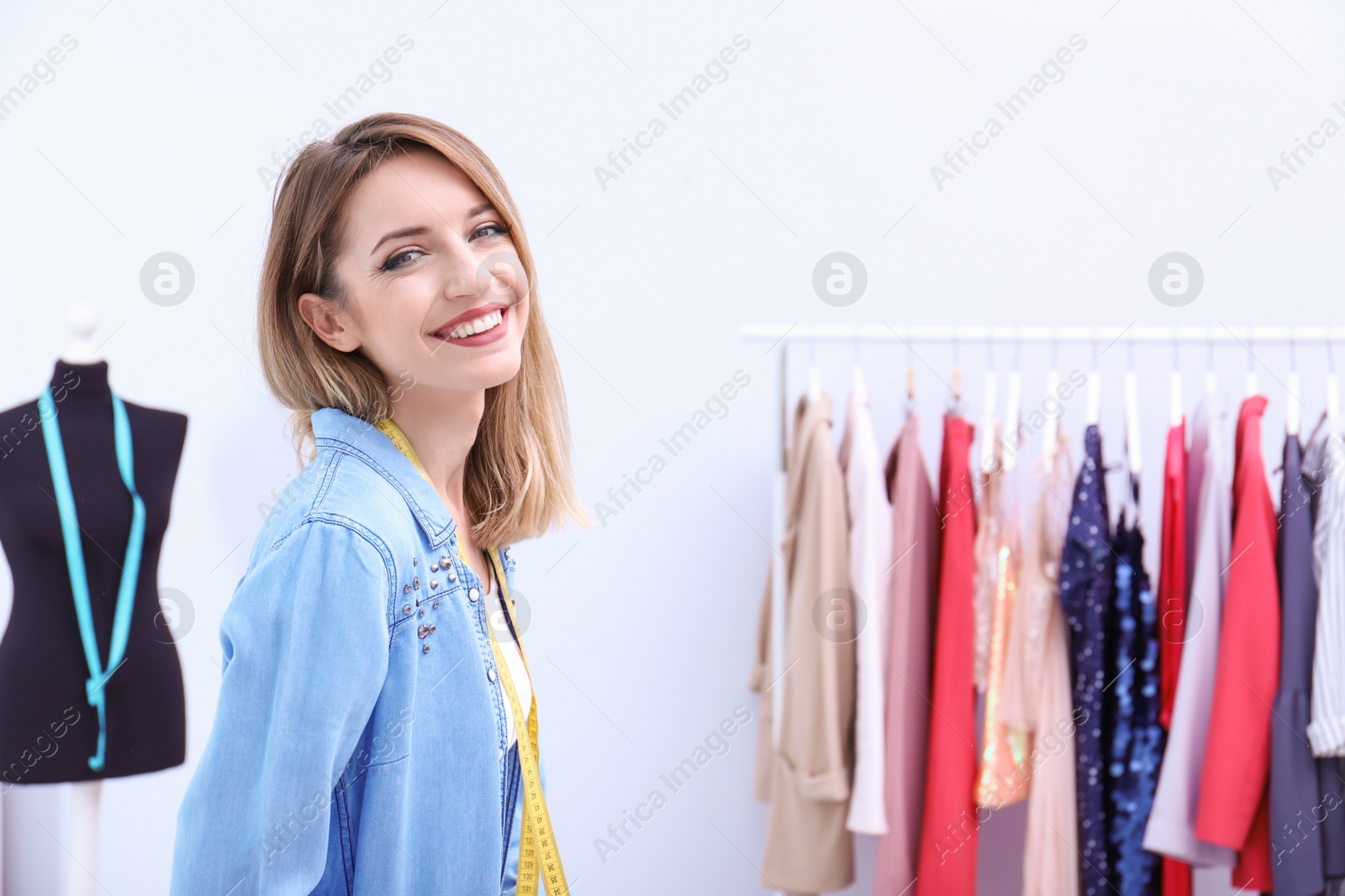 Photo of Beautiful young stylist at workplace near rack with clothes. Space for text