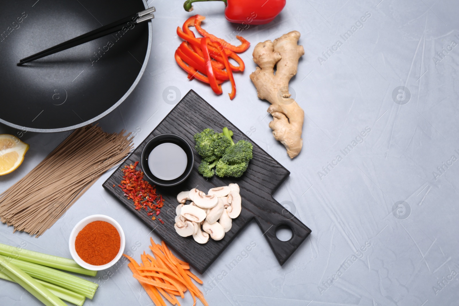 Photo of Wok, chopsticks and different products on grey table, flat lay. Space for text