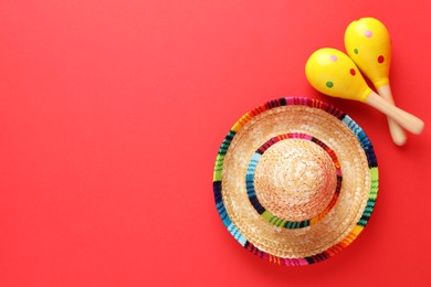 Mexican sombrero hat and maracas on red background, flat lay. Space for text