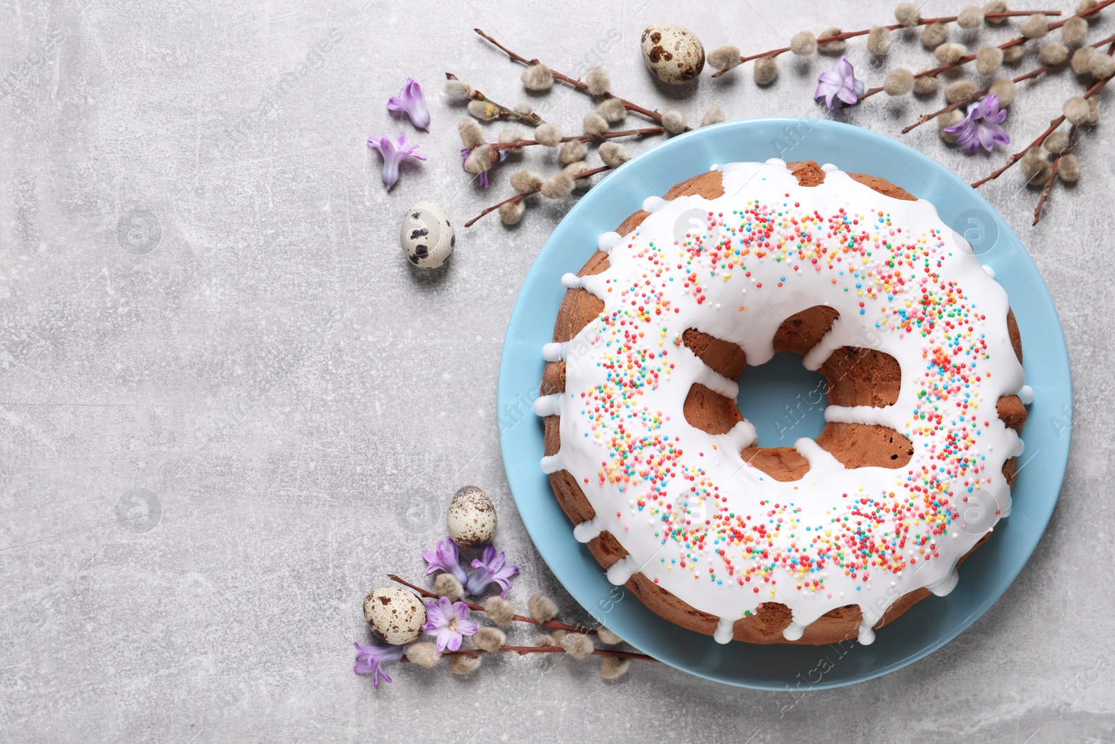 Photo of Glazed Easter cake with sprinkles, quail eggs, flowers and willow branches on light table, flat lay. Space for text
