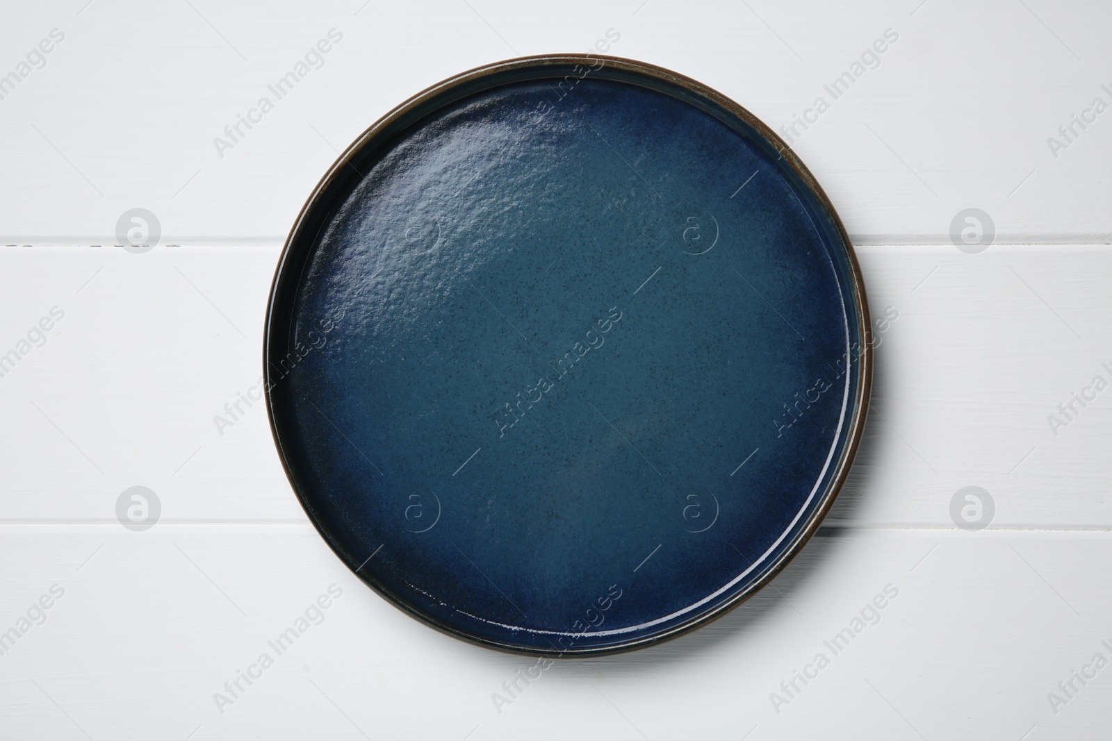 Photo of One dark blue ceramic plate on white wooden table, top view