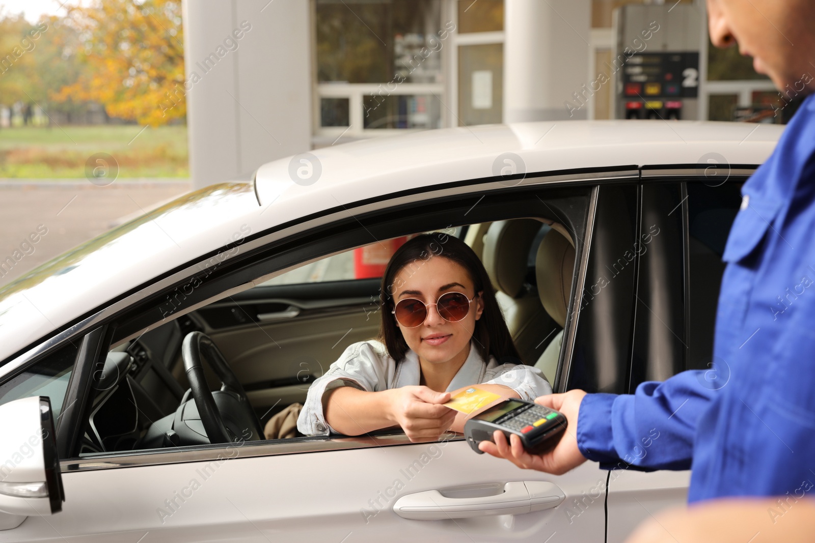 Photo of Woman sitting in car and paying with credit card at gas station