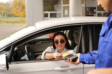 Woman sitting in car and paying with credit card at gas station