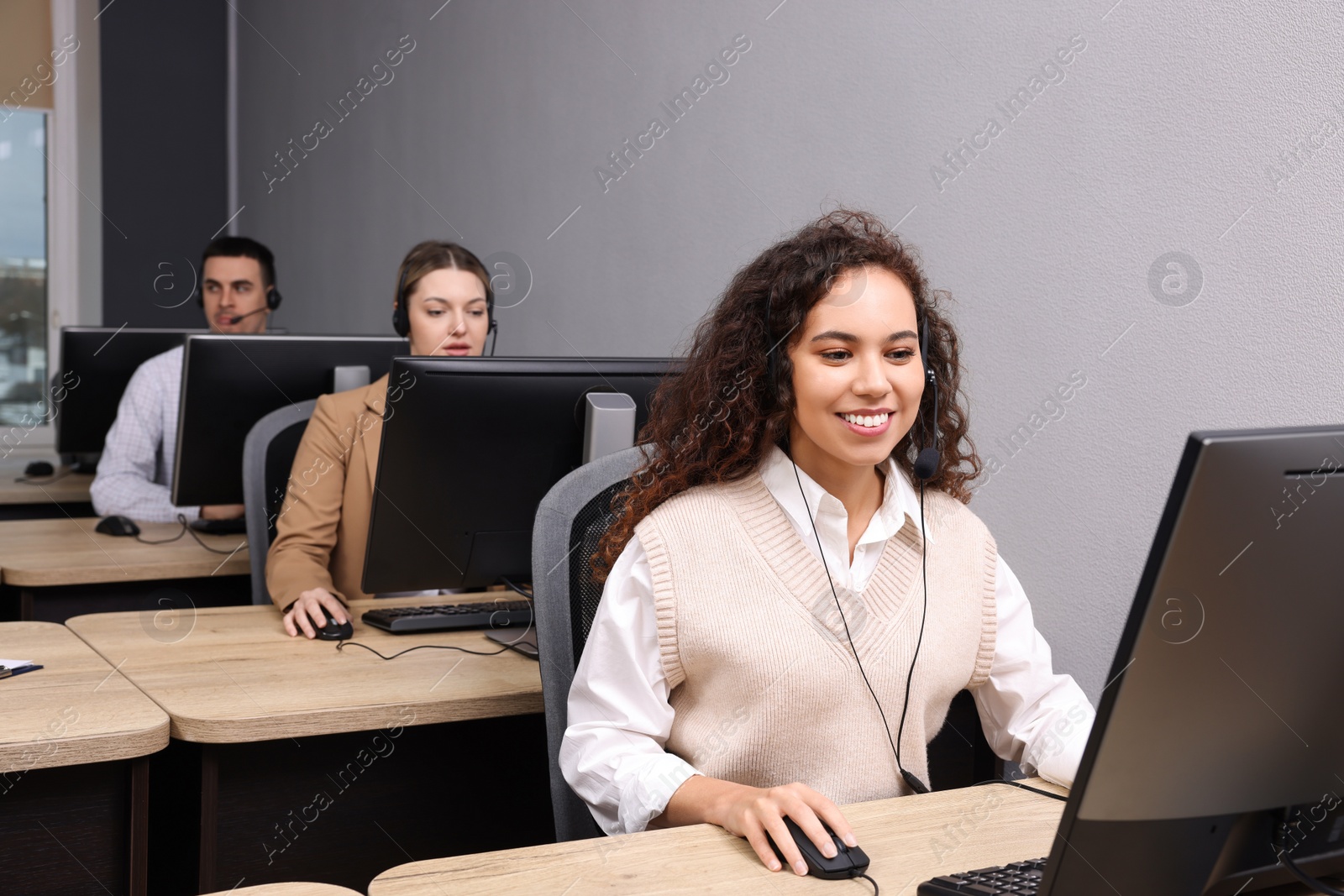 Photo of African American call center operator with headset and her colleagues working in modern office