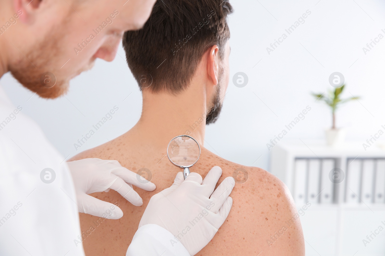 Photo of Dermatologist examining patient's birthmark with magnifying glass in clinic