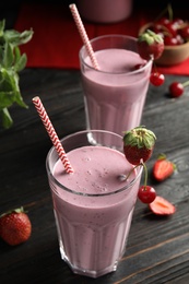Photo of Tasty fresh milk shake with berries on black wooden table, closeup