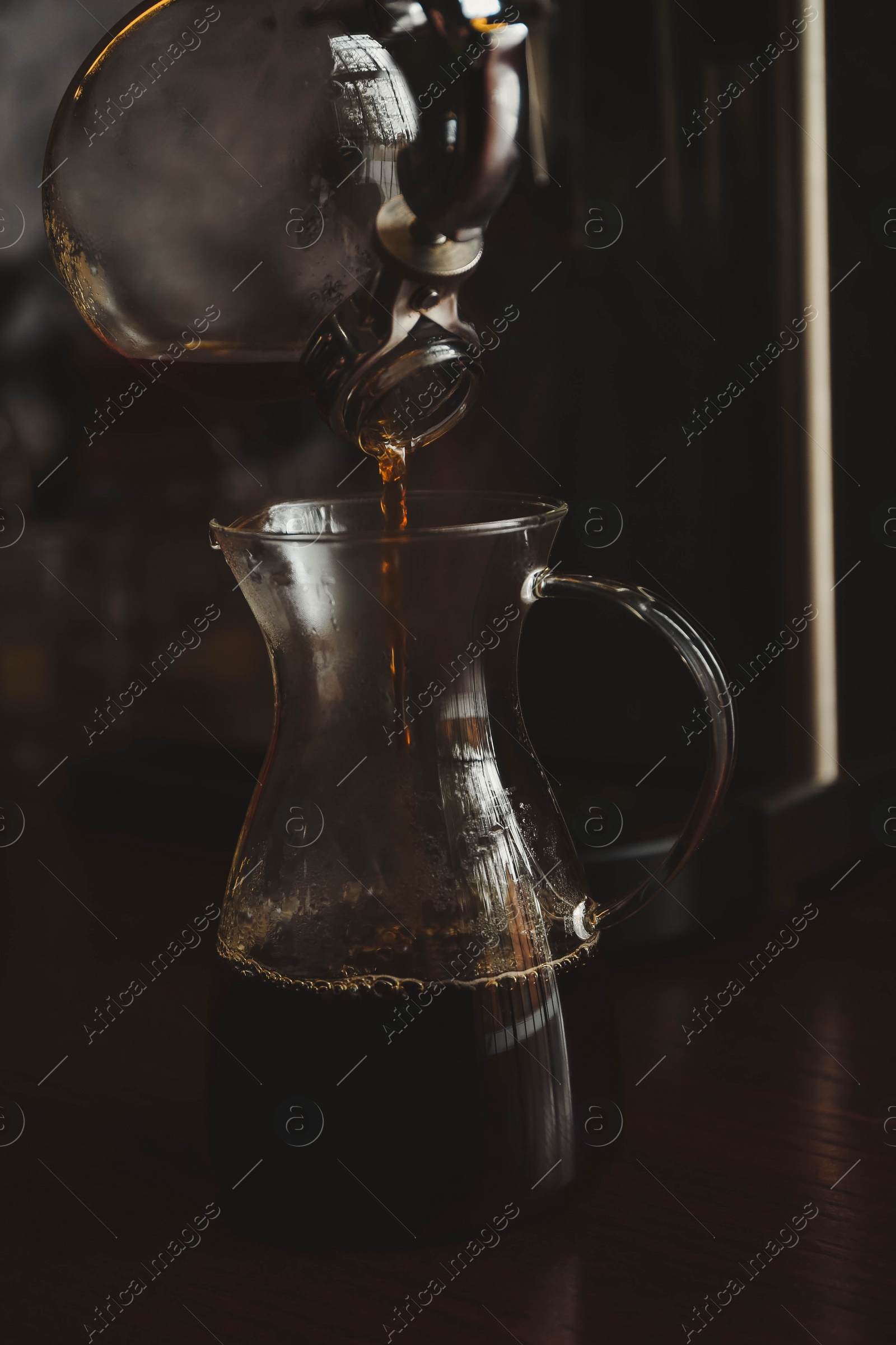 Photo of Pouring coffee into glass jug on wooden table in cafe