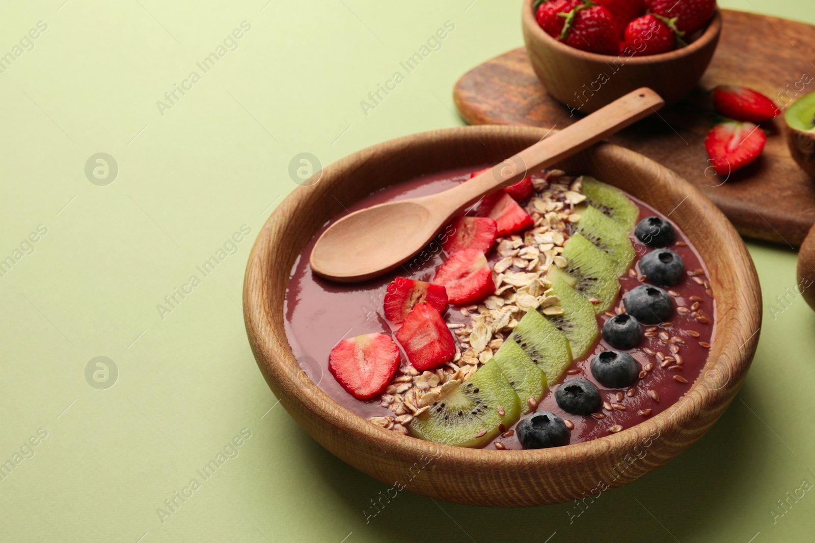 Photo of Bowl of delicious smoothie with fresh blueberries, strawberries, kiwi slices and oatmeal on light green background. Space for text