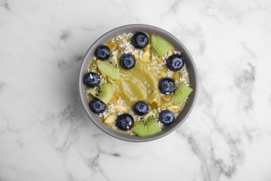 Photo of Bowl of delicious fruit smoothie with fresh blueberries, kiwi slices and coconut flakes on white marble table, top view