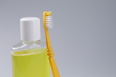 Fresh mouthwash in bottle and toothbrush on grey background, closeup. Space for text