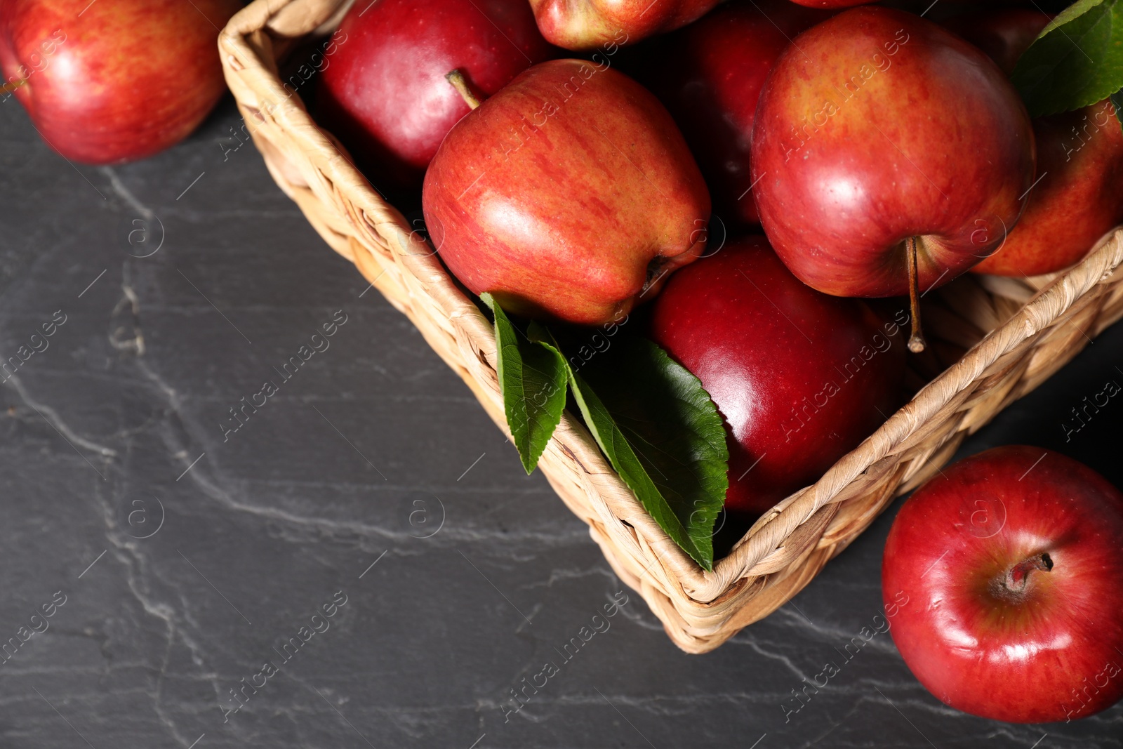 Photo of Fresh red apples and leaves in basket on dark grey table, above view. Space for text