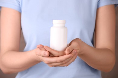 Woman holding blank white bottle with vitamin pills, closeup