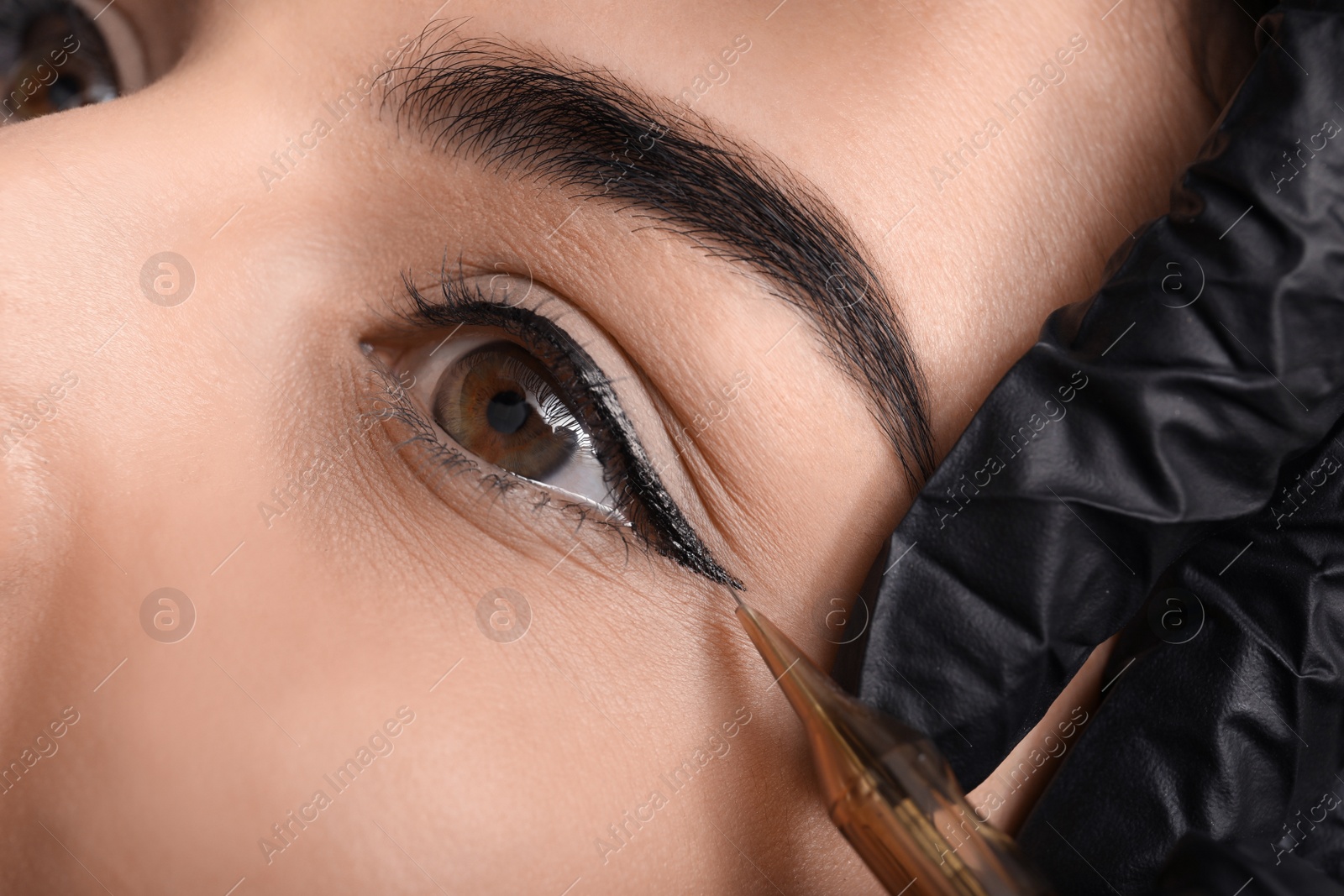 Photo of Young woman undergoing procedure of permanent eye makeup in tattoo salon, closeup