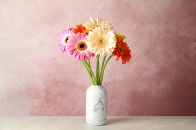 Photo of Bouquet of beautiful bright gerbera flowers in vase on marble table against color background