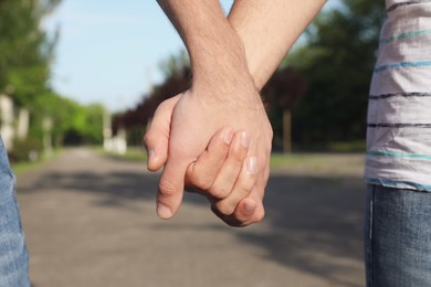 Photo of Gay couple holding hands together in park on sunny day, closeup