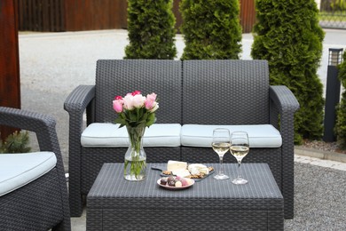 Vase with roses, glasses of wine and food on rattan table on outdoor terrace