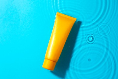 Photo of Tube with moisturizing cream in water on light blue background, top view