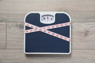 Photo of Scales and measuring tape on wooden background, top view. Weight loss