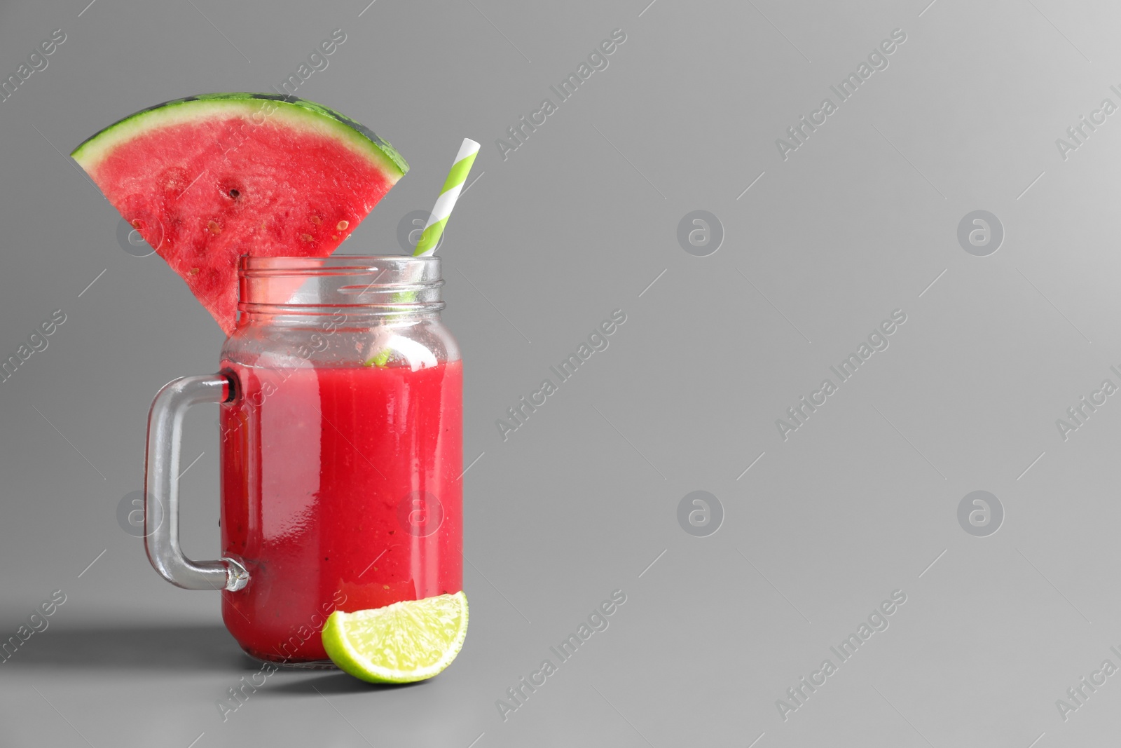 Photo of Tasty summer watermelon drink with lime in glass mason jar on grey background. Space for text