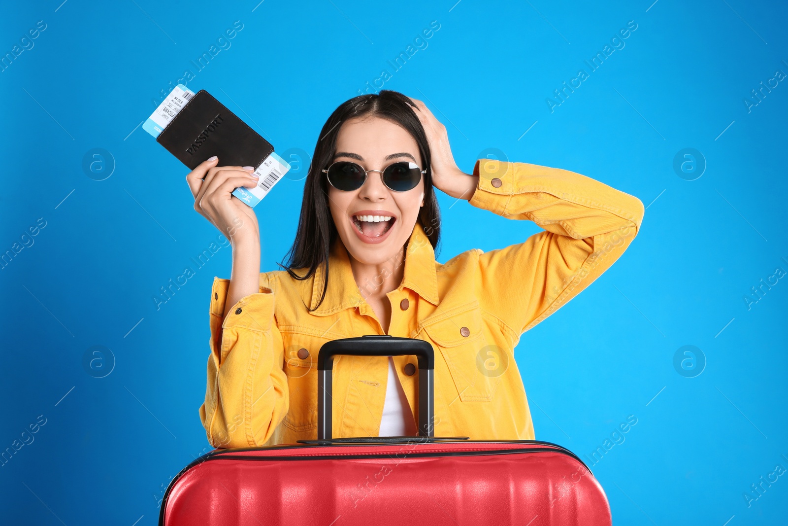 Photo of Beautiful excited woman with suitcase and ticket in passport for summer trip on blue background. Vacation travel