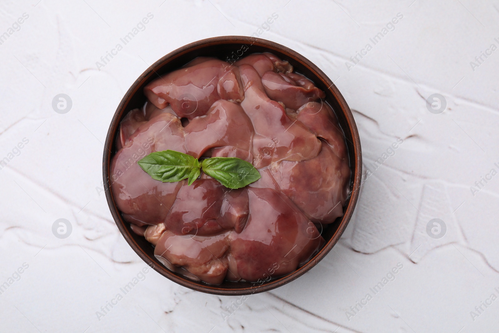 Photo of Bowl with raw chicken liver and basil on white textured table, top view