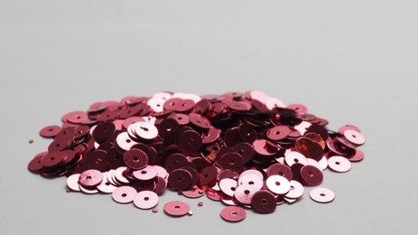 Pile of red sequins on light grey background, closeup