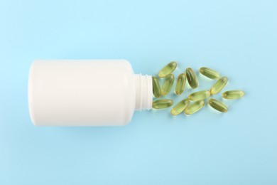 Bottle and vitamin capsules on light blue background, top view