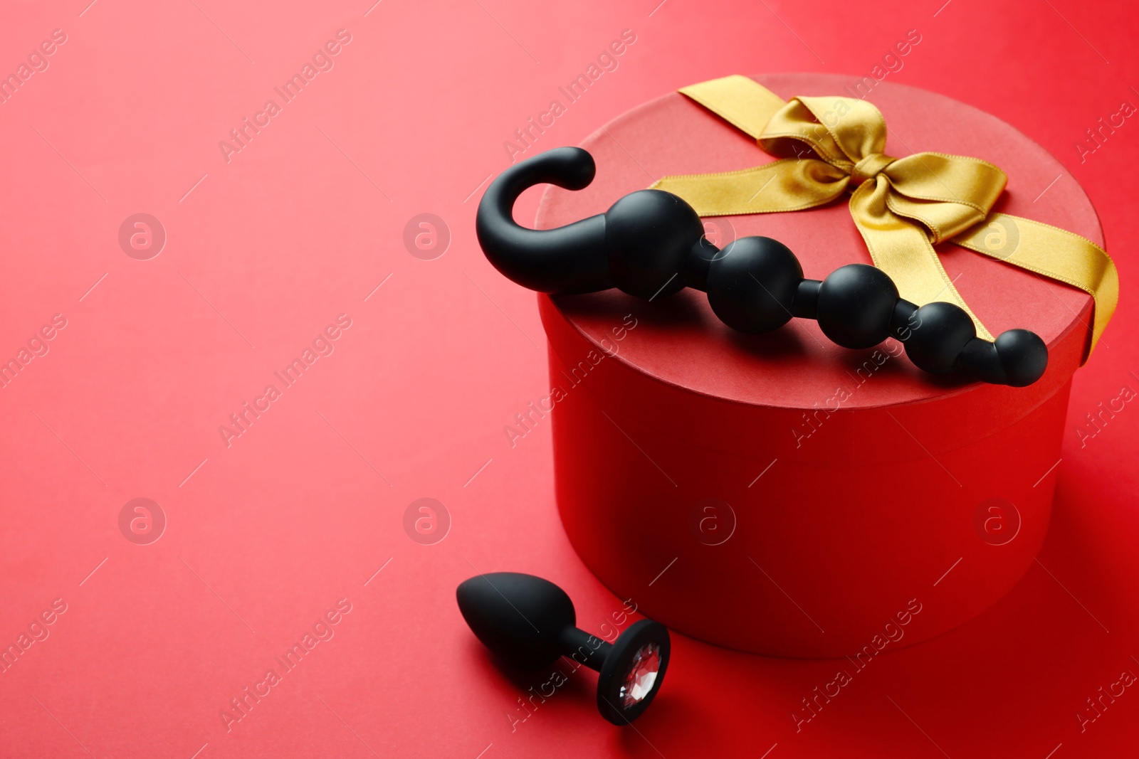 Photo of Gift box with sex toys on red background. Space for text