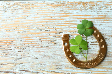 Clover leaves and horseshoe on light wooden table, flat lay with space for text. St. Patrick's Day celebration