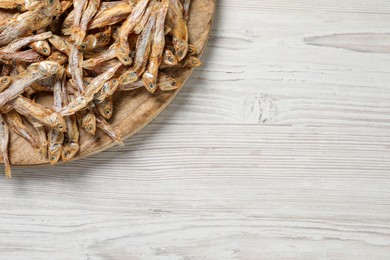 Photo of Plate of tasty dried anchovies on white wooden table, top view. Space for text