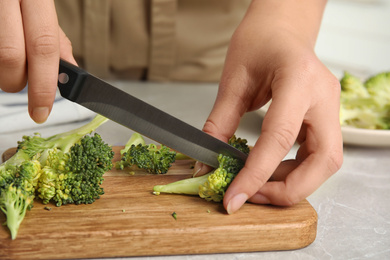 Photo of Woman cutting raw broccoli at light grey marble table, closeup